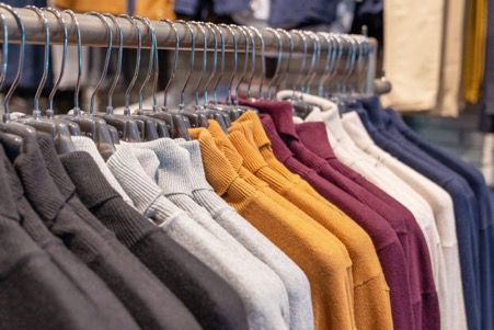 Sweaters and pullovers in different colors, black, gray, white and crimson hang on a hanger in a clothing store in a row. autumn and winter seasonal collection